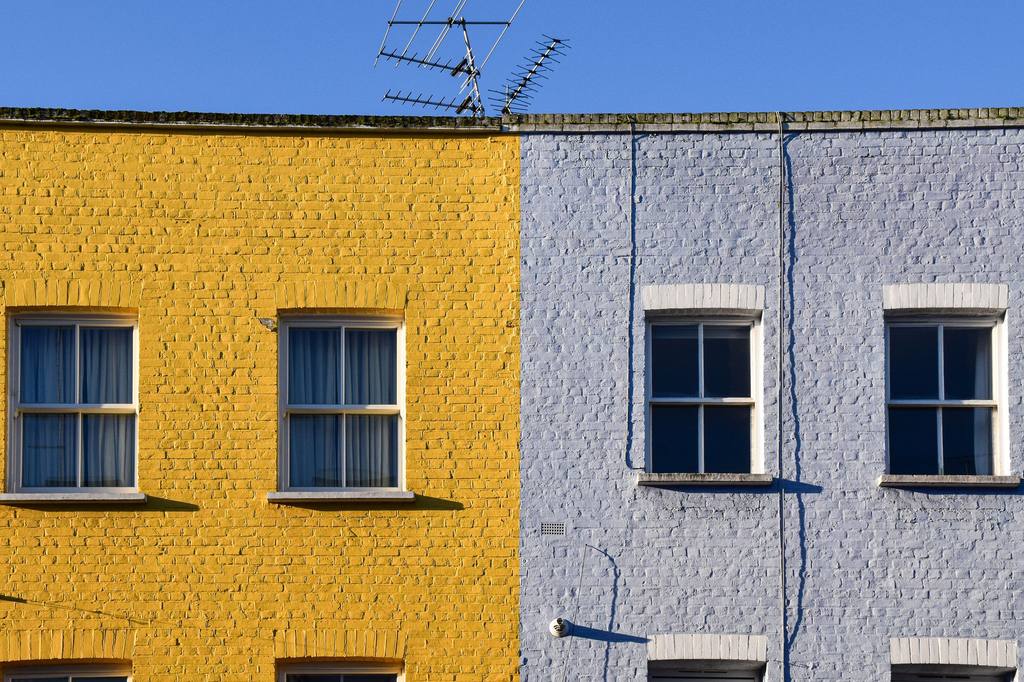 Two painted brick terraced houses in London, one ochre yellow and one pale lilac, with white sash windows